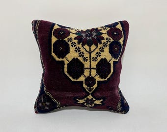 May include: A burgundy throw pillow with a cream and navy blue floral pattern. The pillow is made of a soft, woven fabric.