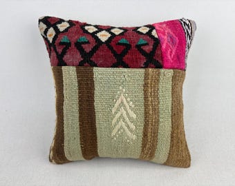 May include: A square throw pillow featuring a top section with a dark red, black, and white geometric pattern and a bright pink accent. The bottom section consists of light green and brown vertical stripes with a central white chevron design.