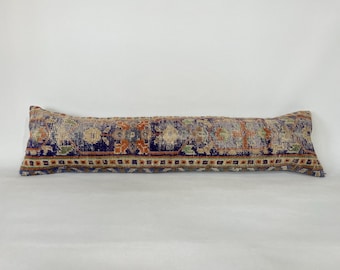 May include: A long, rectangular pillow with a colorful, patterned fabric. The fabric features a blue background with intricate floral and geometric designs in shades of orange, red, green, and beige.