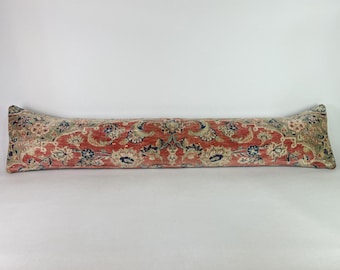 May include: A long, rectangular pillow with a floral pattern in shades of red, beige, and blue. The pillow has a vintage, rug-like appearance, with a central design and decorative edges. The pillow is designed to be placed on the floor or on a bench.