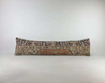 May include: A long, rectangular lumbar pillow featuring a vintage-style woven textile pattern. The design displays a central band of muted orange and beige floral motifs, bordered by intricate dark blue and cream decorative geometric patterns.