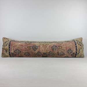 Puede incluir: Un cojín largo y rectangular con un diseño de alfombra vintage. El cojín presenta un campo central rosa descolorido con motivos florales en azul y beige. Los bordes tienen un borde azul oscuro con patrones intrincados. El cojín mide aproximadamente 91 cm de largo.