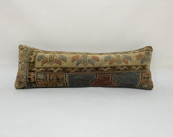 May include: A long, rectangular pillow with a colorful, geometric pattern. The pillow is made of a woven fabric with a soft, textured surface. The colors in the pattern include shades of brown, beige, blue, and red.