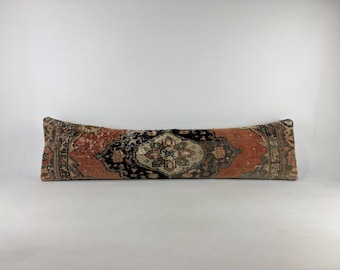 May include: A long, rectangular lumbar pillow featuring a faded, intricate pattern in shades of terracotta, black, and beige. The textile displays a central medallion design with ornate borders, showcasing a weathered, aged appearance throughout.