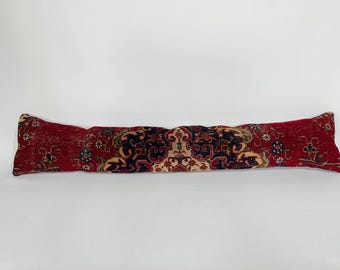 May include: A long, rectangular pillow with a red, patterned design. The pillow features a central section with a complex, ornate pattern in black, beige, and green, flanked by red sections with floral motifs. The pillow is designed for decorative use.