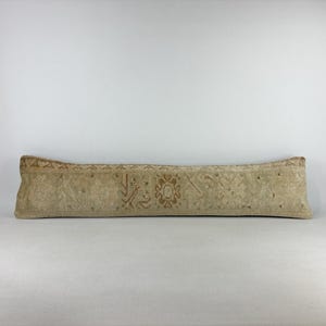 Peut inclure: Un long coussin lombaire rectangulaire présentant un motif textile vintage délavé dans des tons beige clair et brun clair. Le tissu affiche des motifs géométriques et floraux complexes et usés dans des tons terreux sur toute sa surface.