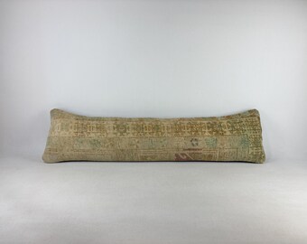 May include: A long, rectangular bolster pillow featuring a faded, multi-colored woven pattern in shades of beige, tan, and muted green. The fabric displays a complex, repeating geometric design reminiscent of an antique rug, with a soft texture.