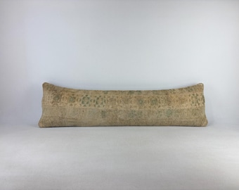 Könnte beinhalten: Ein langes, rechteckiges Lendenkissen mit einem Bezug aus Textil in verblasstem Beige und Hellgrün. Der Stoff zeigt ein abgenutztes, geometrisches Design im Vintage-Stil über die gesamte Länge mit neutralen Tönen und einer strukturierten Optik.