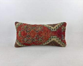 May include: Rectangular decorative pillow with a woven, textured design. The pillow features a central pattern in shades of red, brown, and beige, with geometric borders. The pillow is designed for decorative use.
