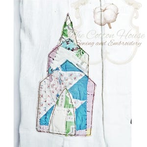 May include: A white fabric item with a colorful patchwork church design. The church features a steeple and is made from various patterned fabrics in shades of blue, green, pink, and white. The text "The Cotton House Sewing and Embroidery" is visible.