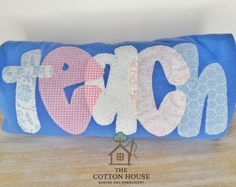 May include: A blue fabric item with the word "teach" appliqued on the front. The letters are in various patterns and colors, including floral, gingham, and honeycomb designs. The Cotton House logo is at the bottom.