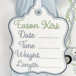 May include: Embroidered tag with the name "Eason Kirk" in green script. The tag has a white polka dot background and space to write the date, time, weight, and length. A white ribbon is attached at the top.