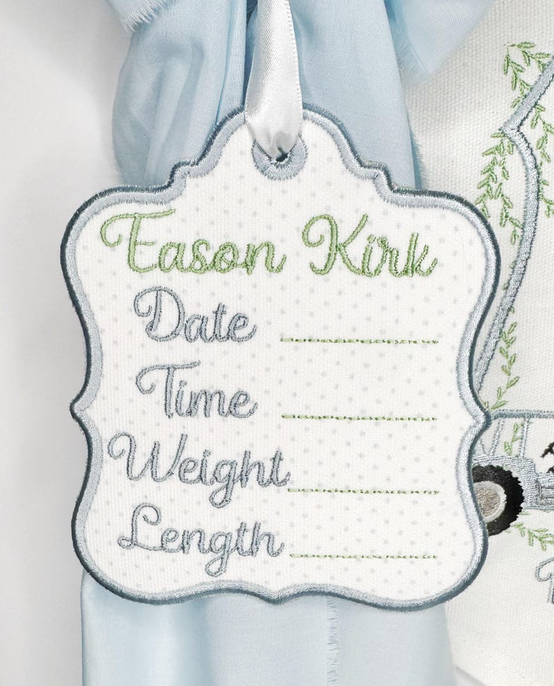 May include: Embroidered tag with the name "Eason Kirk" in green script. The tag has a white polka dot background and space to write the date, time, weight, and length. A white ribbon is attached at the top.