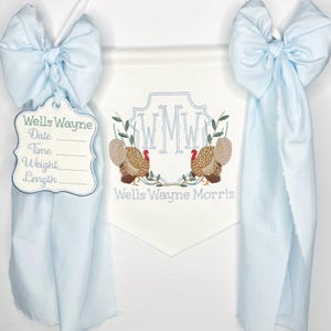 May include: A light blue banner with a white pennant featuring embroidered turkeys and initials. A tag with the name "Wells Wayne" and spaces for date, time, weight, and length hangs from a blue bow.