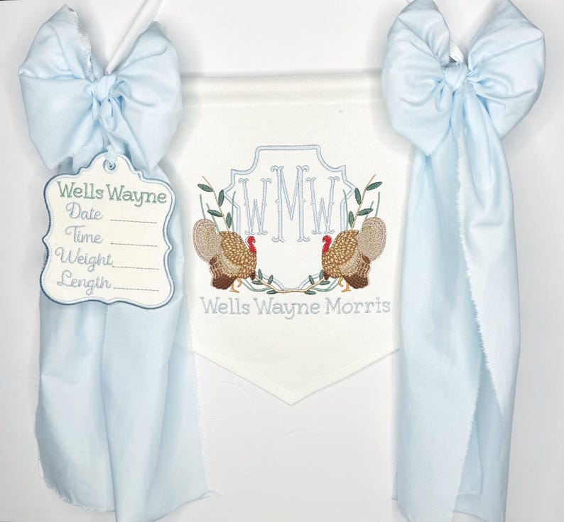 May include: A light blue banner with a white pennant featuring embroidered turkeys and initials. A tag with the name "Wells Wayne" and spaces for date, time, weight, and length hangs from a blue bow.