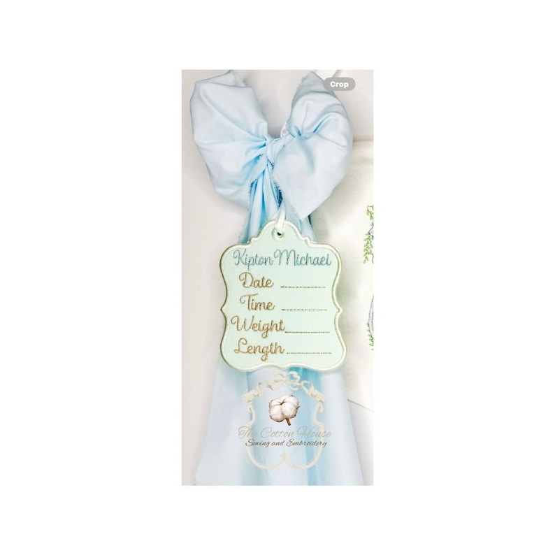 May include: A light blue bow with a decorative tag. The tag is light green with gold trim and has the name "Kipton Michael" and spaces for date, time, weight, and length. The Cotton House logo is at the bottom.