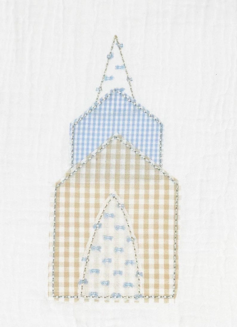 May include: A fabric applique in the shape of a church, featuring a beige and white gingham pattern on the lower section and a light blue and white gingham pattern on the upper section. The edges are outlined with a decorative stitch and small blue accents.