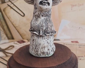 Puede incluir: Una figurita de cerámica de un personaje de hongo con un sombrero de hongo rojo y blanco. La figurita está de pie sobre una base de madera.
