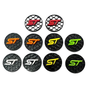 May include: Ten circular emblems featuring the letters "ST" in red, orange, yellow, green, and white. Each emblem has a black honeycomb pattern. The emblems are suitable for automotive use.
