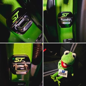 May include: Close-up shots of a car's interior, featuring a green and black ST emblem. The emblem is a hexagonal shape with the letters "ST" in black and green. The car's interior is a bright green color. A Kermit the Frog plush toy is also visible.