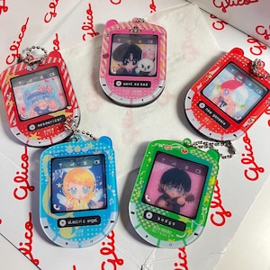 May include: A collection of five colorful keychain pendants designed to resemble retro music players. Each pendant features a different anime-style illustration on its screen, with text like "mesmerizer" and "electric angel". The pendants are red, pink, blue, and green.