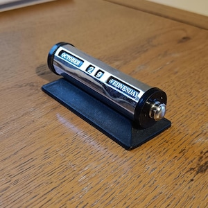 May include: A silver-colored, cylindrical perpetual desk calendar displaying "OCTOBER 29 WEDNESDAY" on a black base. The calendar sits on a wooden surface.