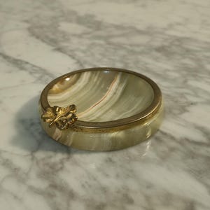 Puede incluir: Un cenicero de m&aacute;rmol verde y blanco con un borde dorado y un dise&ntilde;o de hoja de oro.