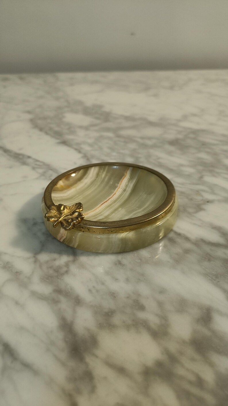Puede incluir: Un cenicero de m&aacute;rmol verde y blanco con un borde dorado y un dise&ntilde;o de hoja de oro.