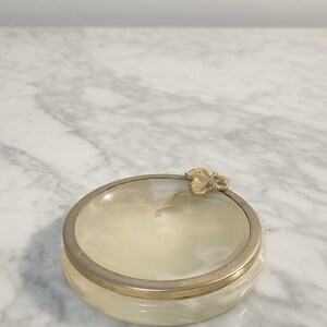 Puede incluir: Un peque&ntilde;o plato redondo de alabastro blanco con un borde dorado y un dise&ntilde;o de hoja de oro.