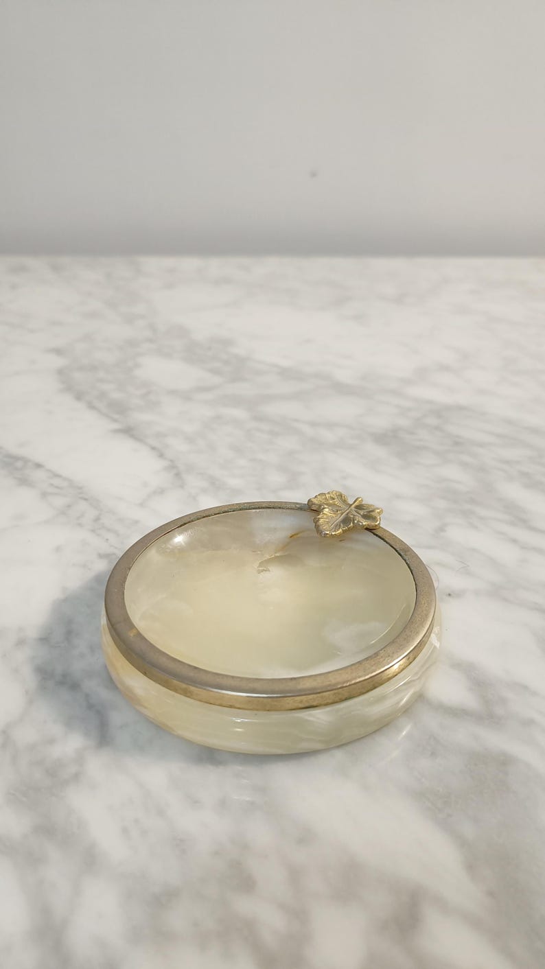 Puede incluir: Un peque&ntilde;o plato redondo de alabastro blanco con un borde dorado y un dise&ntilde;o de hoja de oro.