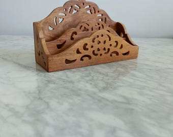 May include: A wooden desk organizer with a natural finish. The organizer has three sections and features intricate cut-out designs along the top and sides. The item is made of wood and is designed to hold letters and other desk items.