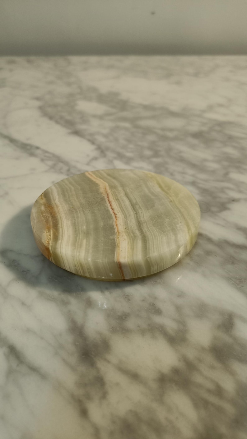 Puede incluir: Un posavasos redondo de m&aacute;rmol verde y blanco con un patr&oacute;n de remolino.
