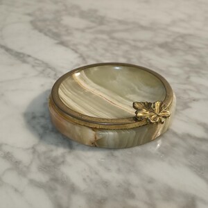 Puede incluir: Un cenicero redondo de m&aacute;rmol verde y blanco con un borde dorado y un dise&ntilde;o de hoja de oro.