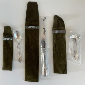 May include: A set of Christofle silver cutlery including a spoon, a knife, and a ladle, each individually wrapped in clear plastic. The set includes three dark olive green velvet storage pouches with labels reading Christofle Sterling Argent 925.