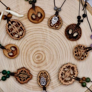 Puede incluir: Una colección de collares hechos a mano con colgantes de madera natural. Los colgantes presentan diseños tallados intrincados y están ensartados en cordones negros con varios acentos de cuentas. Algunos colgantes tienen pequeños amuletos de metal.