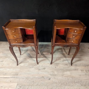 May include: Two antique wooden nightstands with three small drawers each. The nightstands have a dark brown finish, curved legs, and a decorative floral carving on the apron. The interiors are lined with red fabric.
