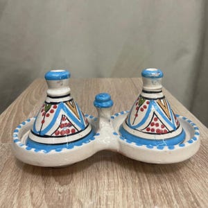 May include: A white ceramic mug with a black handle and the text "But First, Coffee" in a bold, black font. The mug is set against a blurred background, suggesting a cozy setting.