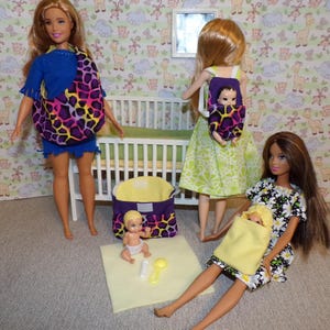 May include: Three dolls are playing with baby dolls. One doll is wearing a blue shirt and a purple and black animal print baby carrier. Another doll is wearing a green dress and a purple and black animal print baby carrier with a baby doll inside. The third doll is wearing a black and white floral dress and a yellow baby carrier with a baby doll inside. There is a white crib in the background.