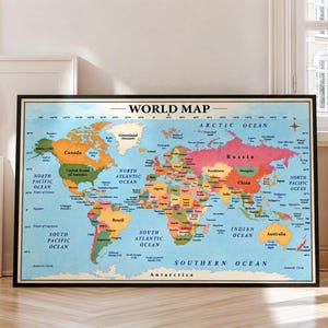 May include: A framed world map poster featuring a light blue ocean background and multicoloured continents. The map displays country names, major bodies of water, and latitude and longitude lines. The text WORLD MAP is printed in black at the top centre.