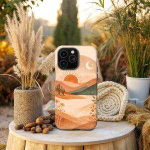 May include: A phone case featuring a desert landscape design with a setting sun, cacti, and mountains in shades of orange, brown, and green. The case has a camera cutout and a smooth finish. The overall theme is nature and travel.