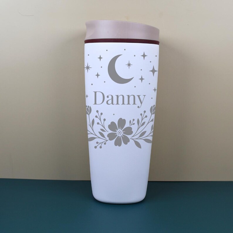 A boho-inspired personalized travel cup with a custom name and delicate floral line art intertwined with celestial motifs, making it a perfect bridesmaid gift or thoughtful keepsake.