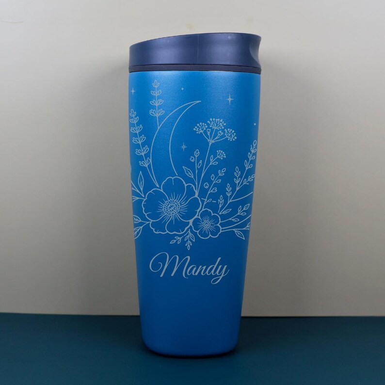 Whimsical engraved Owala SmoothSip bottle decorated with moon and wildflower artwork plus a custom name. The floral celestial design gives this travel coffee cup a soft magical feel, ideal for coffee lovers, nature lovers, and anyone who enjoys personalized gifts with cozy, feminine, and dreamy details.