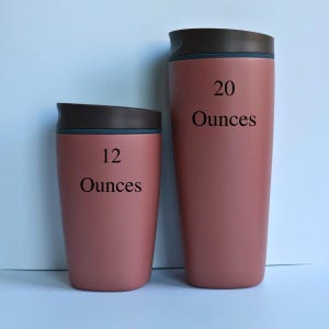 May include: Two insulated travel mugs in a dusty rose color. The smaller mug is labeled "12 Ounces", and the larger mug is labeled "20 Ounces". Both mugs have a dark brown lid with a blue accent. The mugs are designed to keep beverages hot or cold.