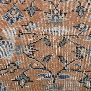 May include: Close-up of a distressed, vintage rug with a warm, earthy color palette. The rug features a repeating floral pattern in shades of rust, blue, and cream, with intricate details and a worn texture. The design has a classic, traditional feel.