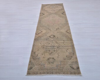 May include: A beige runner rug with a faded floral pattern. The rug has a fringed edge and is made of a soft, woven material.