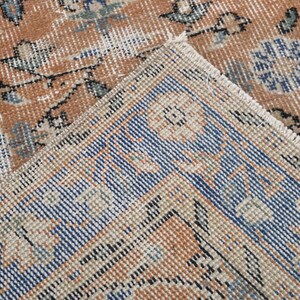 May include: Close-up of a section of a vintage rug with a distressed, faded appearance. The rug features a warm, earthy color palette with shades of brown, beige, and blue. The design includes floral and geometric patterns, with a visible fringe.