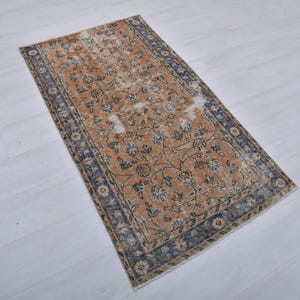 May include: Rectangular rug with a distressed, vintage look. The rug features a central field of warm orange with floral patterns in blue and cream. A dark blue border frames the design, adding contrast. Ideal for living rooms or bedrooms.