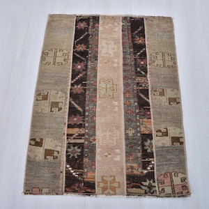 Può includere: Tappeto rettangolare con un design patchwork. Il tappeto presenta strisce verticali nei toni del beige, marrone e rosa. Sono incorporati motivi geometrici e floreali. Il tappeto è probabilmente realizzato in tessuto tessuto.