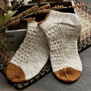 May include: A pair of knitted socks in a white and brown colour scheme. The socks have a textured pattern and a contrasting brown cuff.