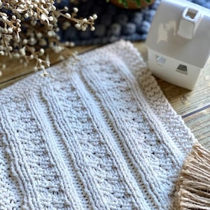 Könnte beinhalten: Ein weißer, gestrickter Geschirrtuch mit Fransenrand. Der Geschirrtuch hat ein strukturiertes Muster und ist aus Baumwolle.